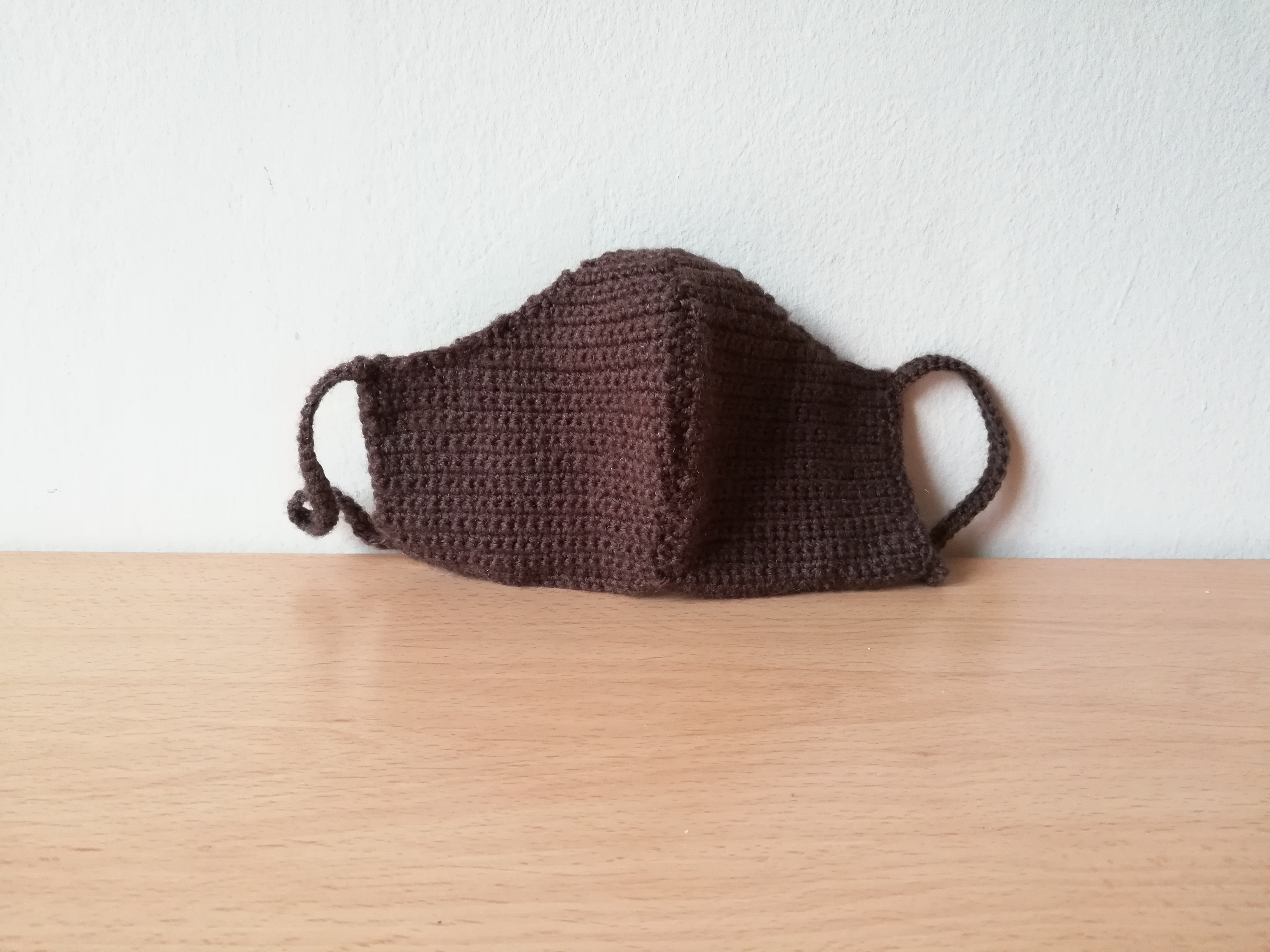 Women-sized Brown Crochet Face Mask on a light brown table against a white wall