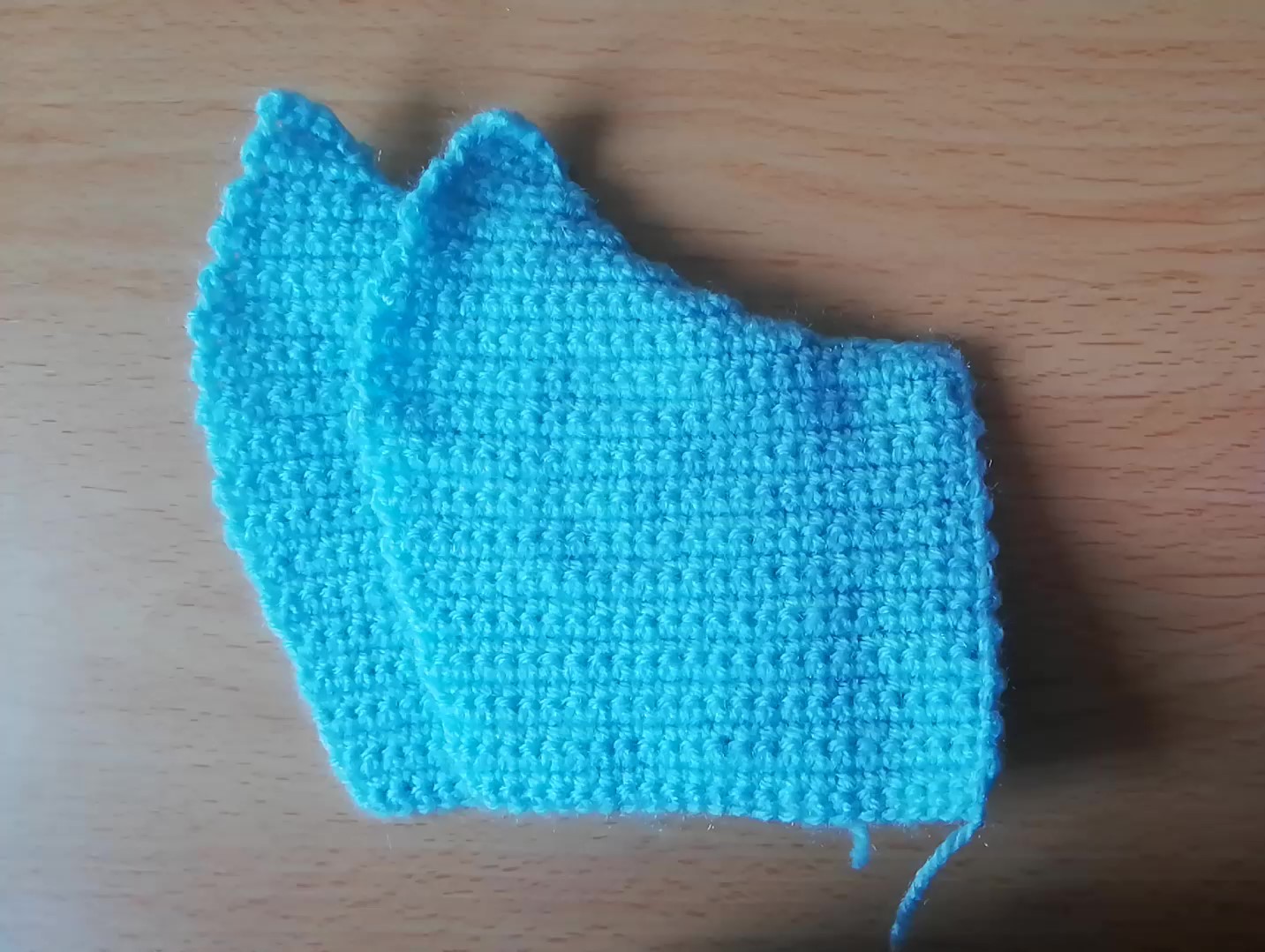 Two halves of the crochet face mask done in turquoise yarn