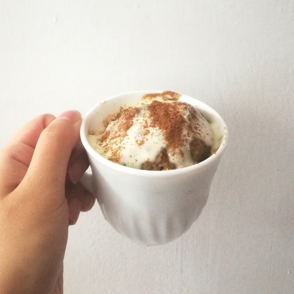 Eggless Cinnamon Mug Cake topped with cream cheese frosting and ground cinnamon