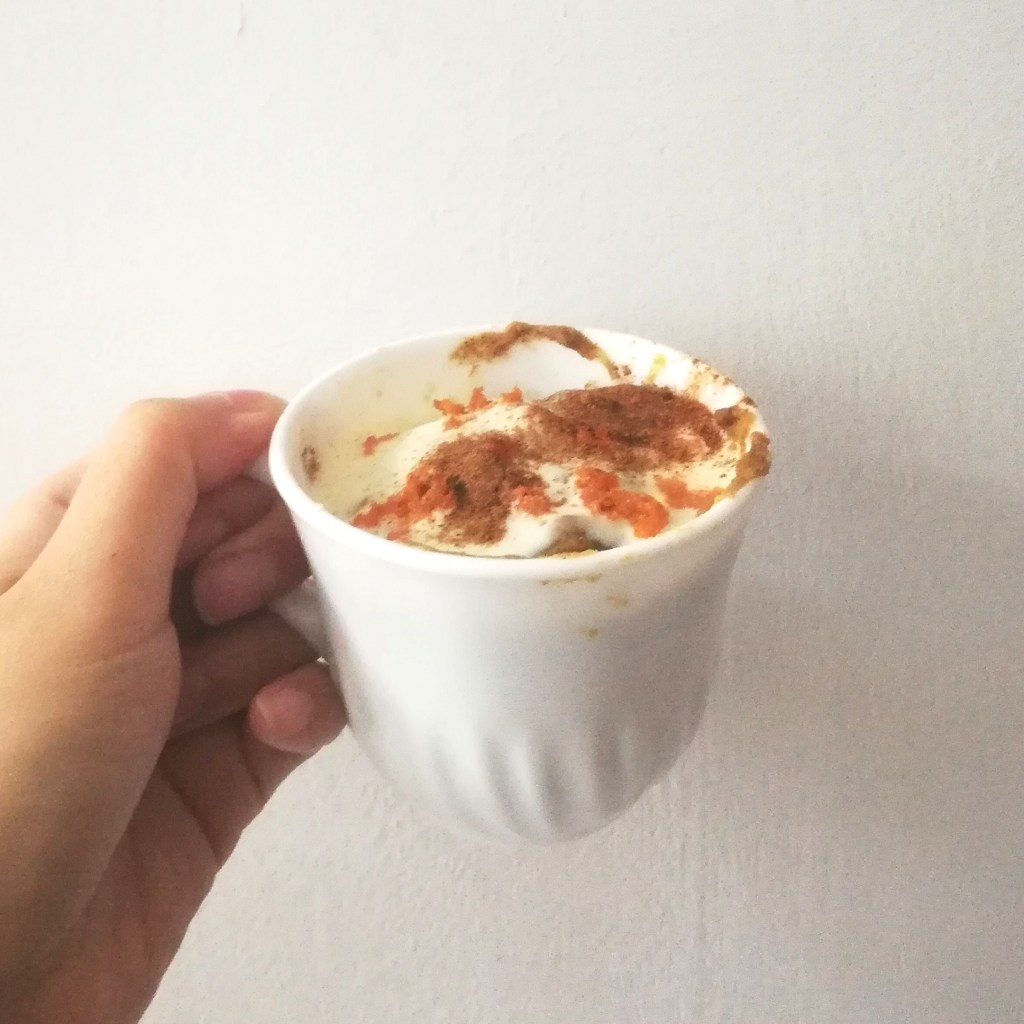 Eggless Carrot Banana Mug Cake topped with cream cheese frosting, shredded carrots, and ground cinnamon